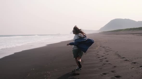 Young Woman Runs on a Black Volcanic Beach Along the Ocean