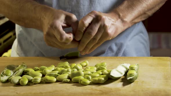 Wide, slider shot from right to left of a cutting board with shelled fava beans on the board and a m