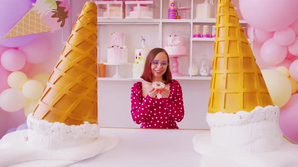 Young Woman in Red Dress with Donut Standing in Decorative Confectionery