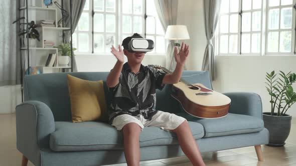 Asian Boy Sitting On Sofa And Testing New Virtual Reality Headset Device