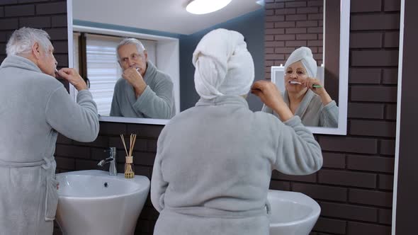 Senior Couple Grandmother and Grandfather Brushing Teeth and Looking Into a Mirror at Bathroom