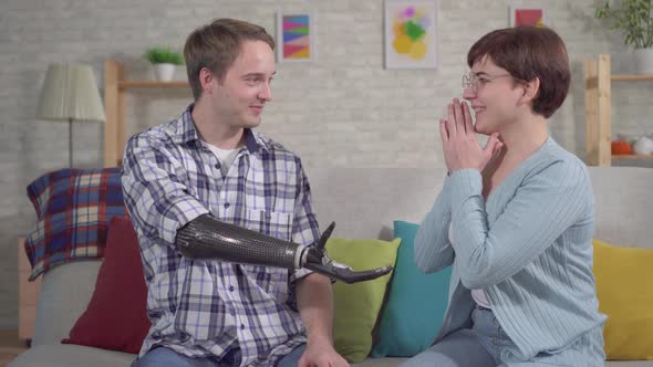 Young Man with a Cyber Prosthetic Hand Holds an Engagement Ring and Proposes To His Girlfriend