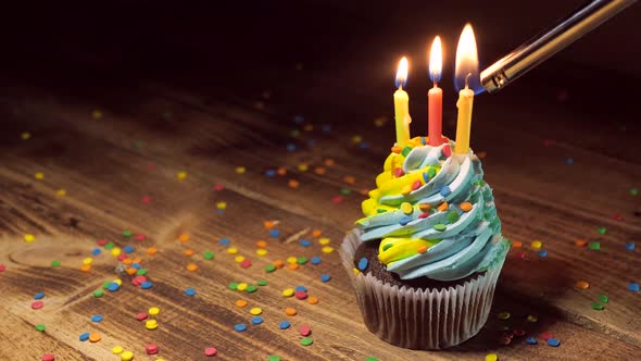 Birthday Cupcake with Blue and Yellow Cream Icing and Lit Candles on a Wooden Table