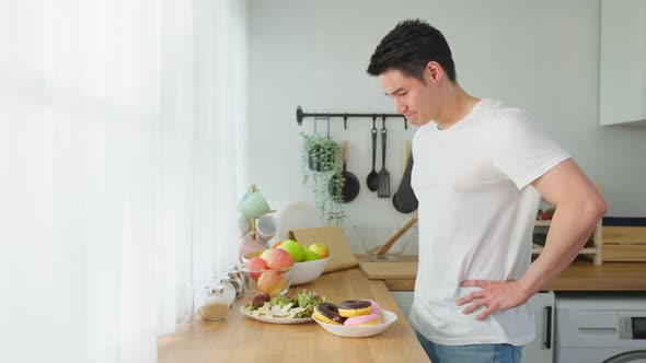 Asian young attractive handsome male eating green salad in kitchen at home.