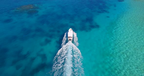 Aerial drone view of a motor boat going to a scenic tropical island in the Maldives.