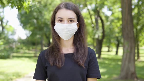 A Young Turkish Woman Takes Off a Face Mask and Smiles at the Camera in a Park on a Sunny Day