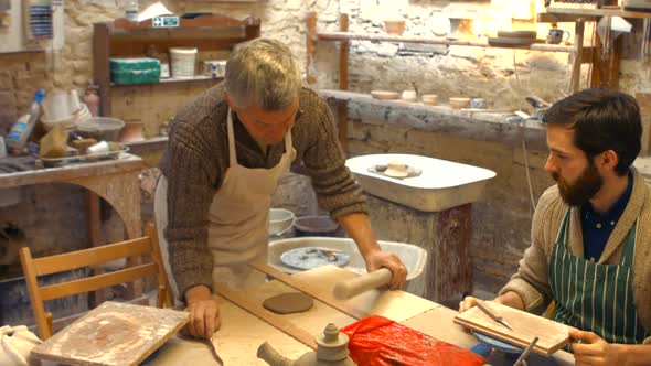 Potter teaching his colleague to roll the clay