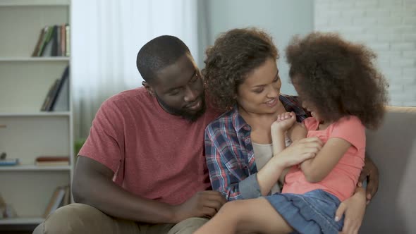 Mother tickling and amusing her little daughter, family sitting on couch