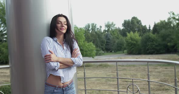 Girl Stands Outdoors Crosses Hands Looks Around with Smile and Corrects Hair