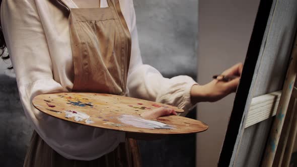 Young Woman Mixing Colors on the Palette with a Brush and Applying in on the Canvas