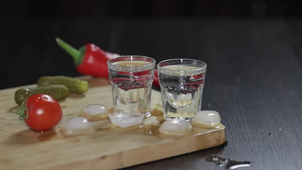 Vodka in Shot Glasses on Rustic Wood Board. Adding Ice Cubes.