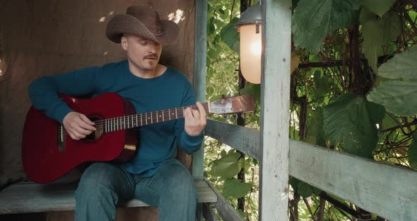 Man with an Acoustic Guitar is Sitting on Porch of House Playing an Instrument