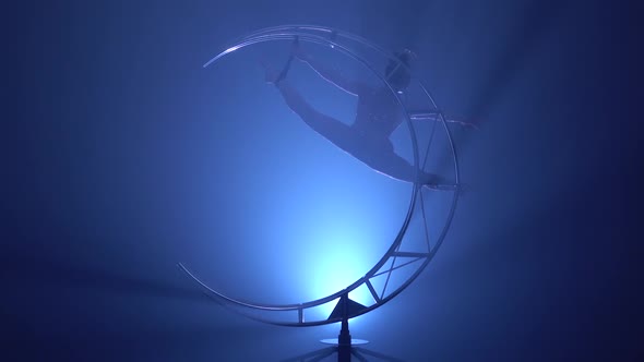 Gymnast in a Brilliant Costume Performs Tricks on a Special Design . Blue Smoke Background