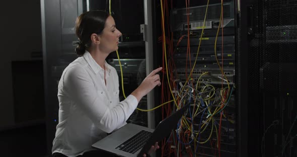 Caucasian female it technician using laptop, pointing and checking computer server