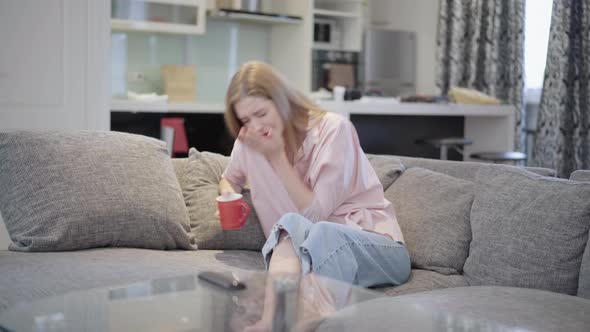 Young Slim Ill Woman Sneezing Sitting on Couch in Living Room