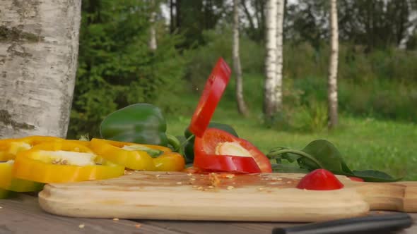 Slices of Fresh Ripe Pepper Fall on a Wooden Board in Slow Motion