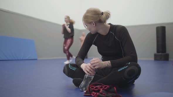 Portrait Cute Athletic Woman Sitting on the Floor in the Gym Resting After Training Drinking Water