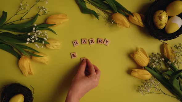 Top view of hands putting together scrabble letters as Happy Easter in the frame yellow eggs along w