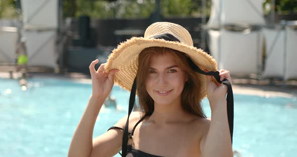 Beautiful Young Brunnete Girl in Straw Hat Smiling at Camera Near Pool