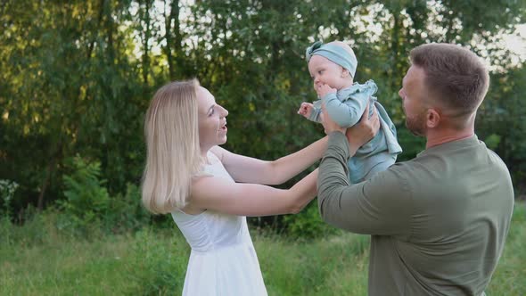 Happy Couple Plays with Baby Daughter on Lawn in Park