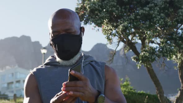 Senior african american man wearing face mask exercising putting earphones in