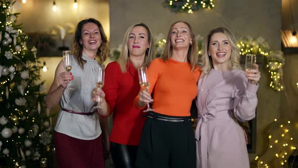 Four Women in Elegant Clothes Hold Glasses of Sparkling Wine Hugged and Dance Near the Christmas