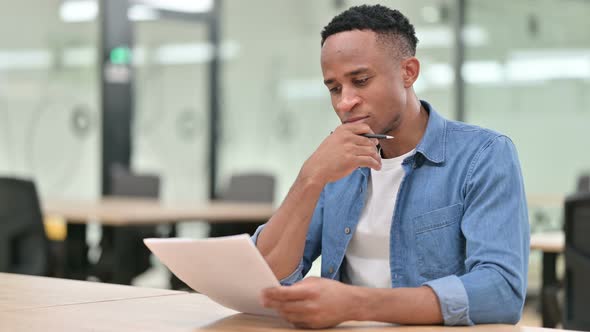 Focused Casual African Man Reading Documents in Office 