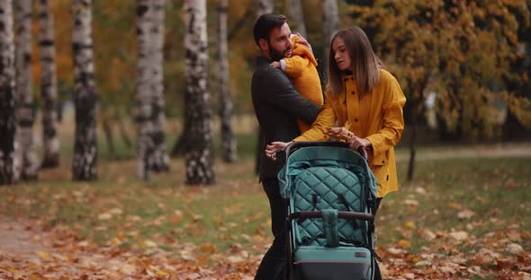 Young Family Walking with Baby Carriage at the Autumn Park