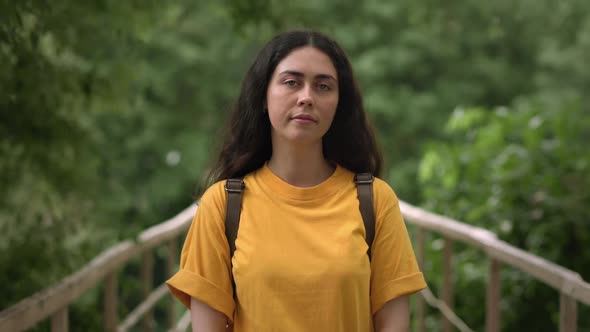 Portrait of a young smiling Caucasian woman against the background of a park and a bridge.