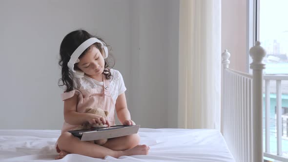 Cute Asian pre-school aged girl listening to music on the bed