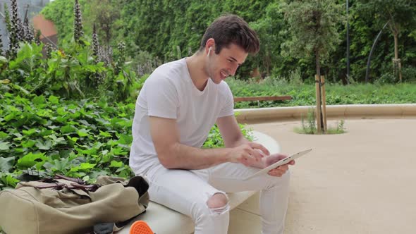 Handsome Young Hispanic Man Using Digital Tablet in City Park