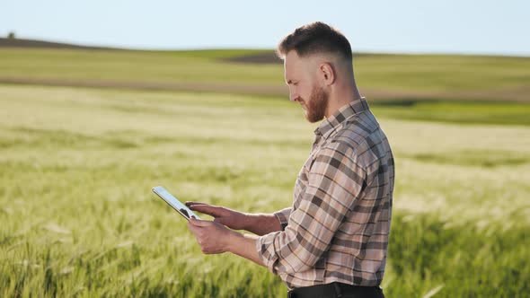 The Farmer is Standing Near the Field and Working with a Tablet