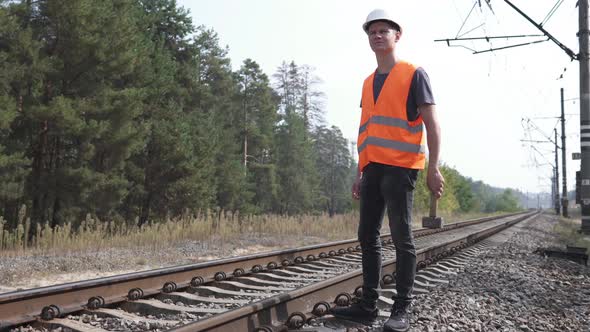 The railway worker stands along the railway tracks, holding a sledgehammer in his hands.