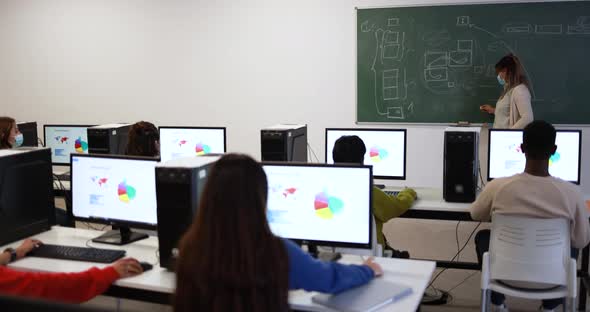 Young multiracial students and teacher wearing safety face masks inside computer classroom