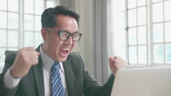 Winning Asian Businessman Looking At Computer Screen While Working At Home