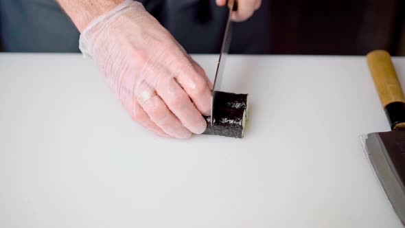 Male Chef Hands Cutting Prepared Maki Sushi Roll on Board in Restaurant Kitchen