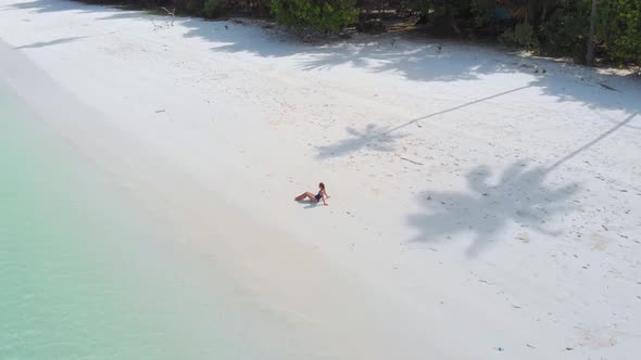 Aerial: Woman relaxing on white sand beach turquoise water tropical coastline