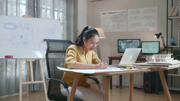 Asian Woman Engineer With A Laptop Drawing Blueprint At The Office