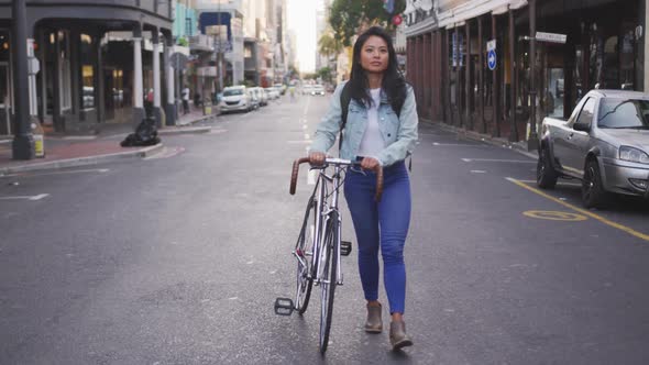 Mixed race woman walking next to her bike on the street