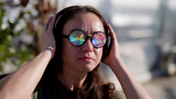 Adult Woman with Crazy Crystal Glasses is Enjoying Music By Wireless Headphones on City Street