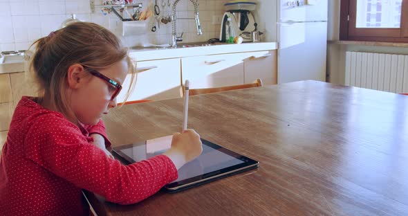 Little Girl Drawing on Tablet at Home. Child Drawing on Tablet Device in Kitchen on Distance
