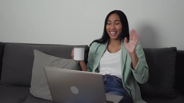 Young woman doing video call using laptop while drinking cup of tea at home