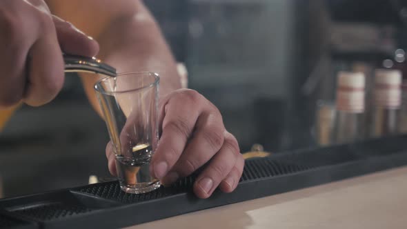 Section of Unrecognizable Bartender Pouring Alcohol Shots at Bar Counter to Little Glasses of Blue