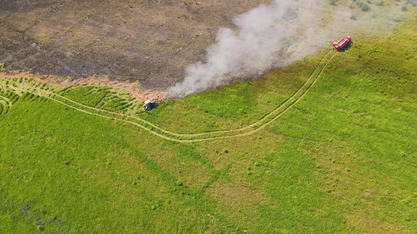 At the Edge of the Fire in the Field a Tractor and a Fire Engine Smoke Swirls