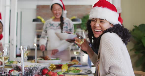 Happy mixed race woman in santa hat celebrating meal with friends at christmas time