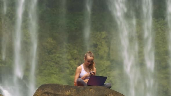 Girl Sits with Laptop and Phone on Cliff at Water