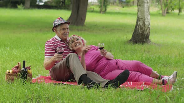 Family Weekend Picnic in Park. Active Senior Old Caucasian Couple Sit on Blanket and Drink Wine