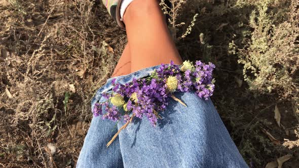 The girl sits on the grass with a bouquet of flowers in jeans. Fashion 90s sneakers, jeans, style.