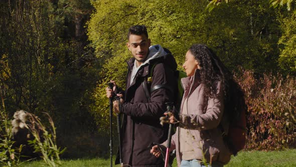 Happy Young Hispanic Couple Guy and Girl Tourists Walking in Forest on Hike with Backpack Doing