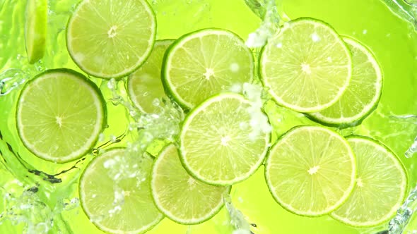 Super Slow Motion Shot of Lime Slices Falling Into Water on Green Background at 1000Fps.